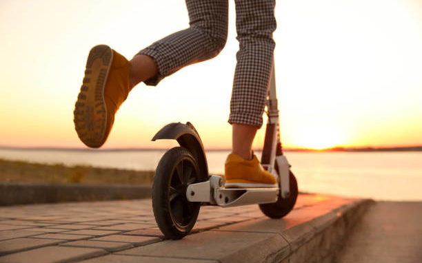 Woman riding electric kick scooter outdoors at sunset, closeup